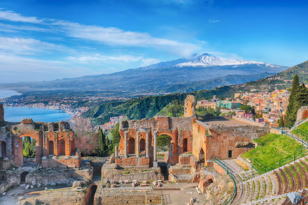 Ruins of ancient Greek theater in Taormina and Etna volcano in the background.
